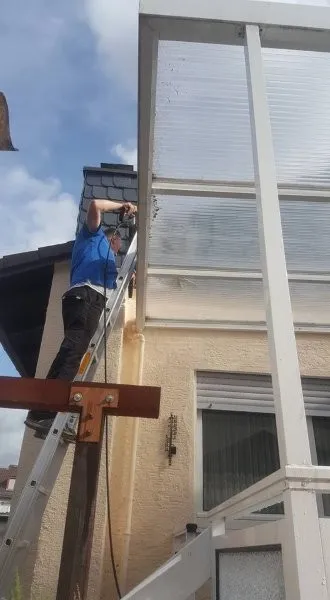 Mitarbeiter reinigt eine Glasdachkonstruktion manuell von einer Leiter aus