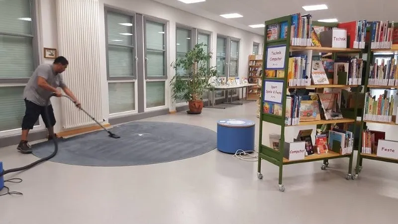 Unterhaltsreinigung in einer Bibliothek mit Teppichreinigung durch einen Mitarbeiter